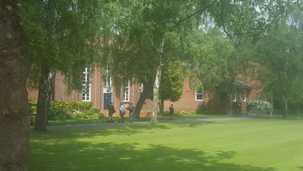 Schüler spazieren auf einem Pfad beben einem roten Gebäude umgeben von Bäumen.