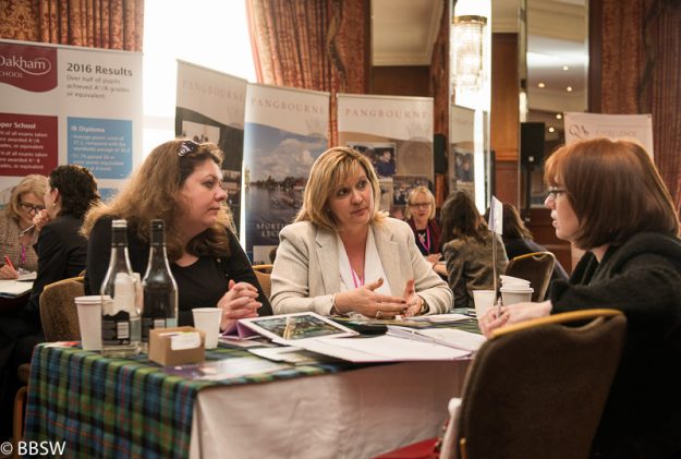 Drei Frauen sitzen am Tisch bei einer Messe und unterhalten sich.