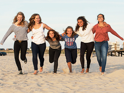 Sechs Schülerinnen umarmen sich und laufen zusammen auf dem Strand