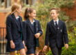 Drei junge Schüler*innen in Schuluniform unterhalten sich draußen.